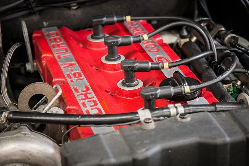 White Ford Escort RS Cosworth with its iconic double rear wing on a misty mountain road in Wales at dawn