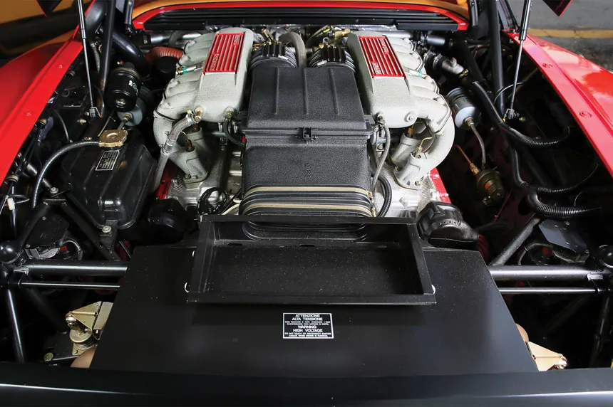 A Ferrari Testarossa flat-12 engine displayed on an engine stand in a clean, professional workshop