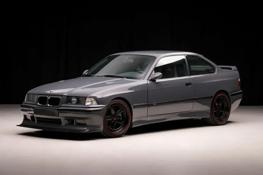 BMW M3 E36 de AC Schnitzer en taller profesional con iluminación dramática y herramientas de trabajo, atmósfera nostálgica del tuning alemán de los años 90