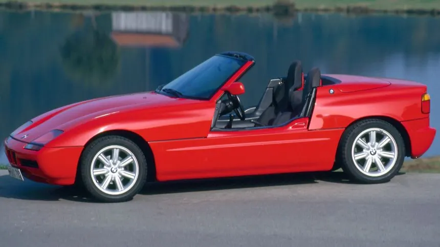 Red BMW Z1 roadster with both sliding doors dropped into the sills, showcasing the unique vertical drop-down door mechanism and open interior, photographed from a dynamic three-quarter rear angle.