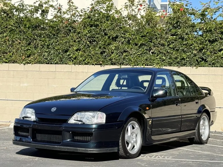  Dark navy Opel Lotus Omega on a wet motorway at night, its understated body kit, specific 17-inch alloy wheels and four exhaust pipes hinting at the 377 bhp twin-turbocharged straight-six beneath the hood.