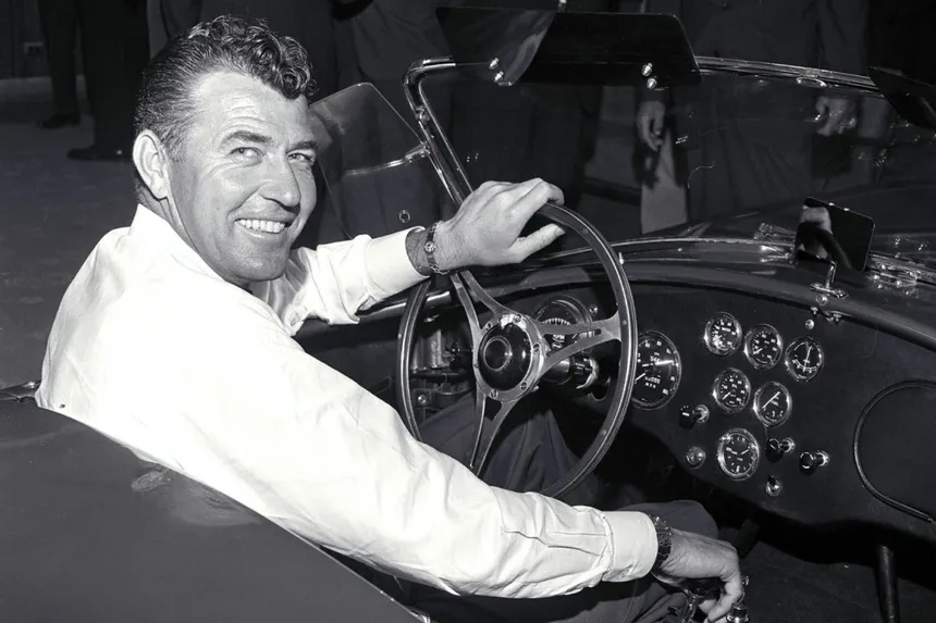 Carroll Shelby con sus monos de granjero de rayas y sombrero Stetson junto a un Shelby Cobra azul en los años 60