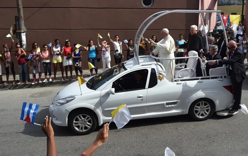 Papamóvil blanco con cúpula de cristal blindado elevada sobre plataforma, rodeado de multitud, iluminación dramática ceremonial