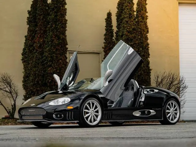 2000 Spyker C8 Spyder photographed in a dark studio, Dutch hand-built mid-engined supercar with scissor doors open revealing exposed gear linkage and brushed aluminium cabin with aviation-style toggle switches, the first modern Spyker after 75 years of silence
